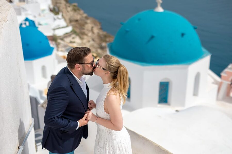 A couple on a blue-domed terrace above Oia at sunrise